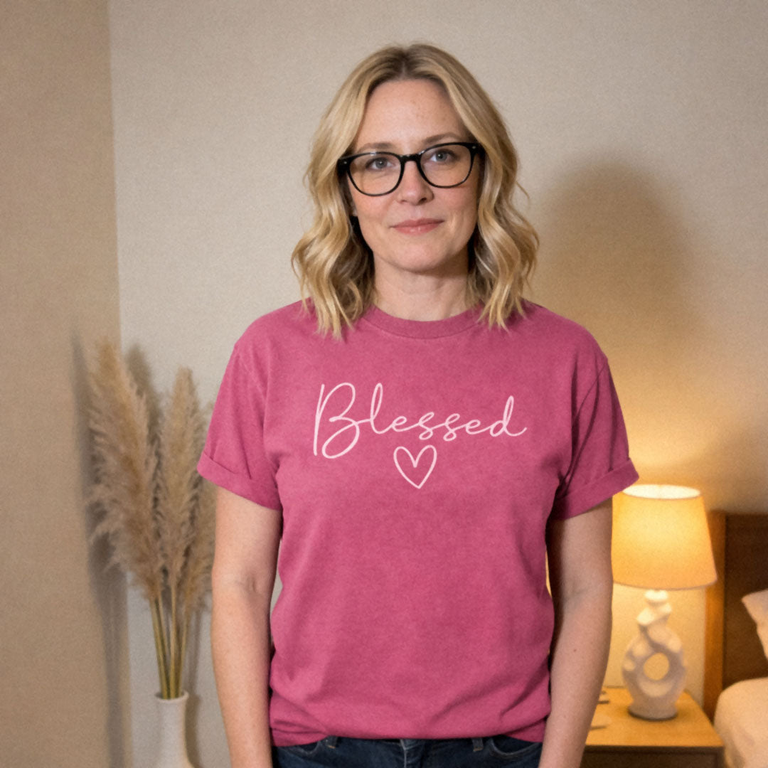 Woman standing in bedroom wearing jeans and a pink (Crunchberry) Comfort Colors 1717® tee with a Blessed handwritten script with a heart design.