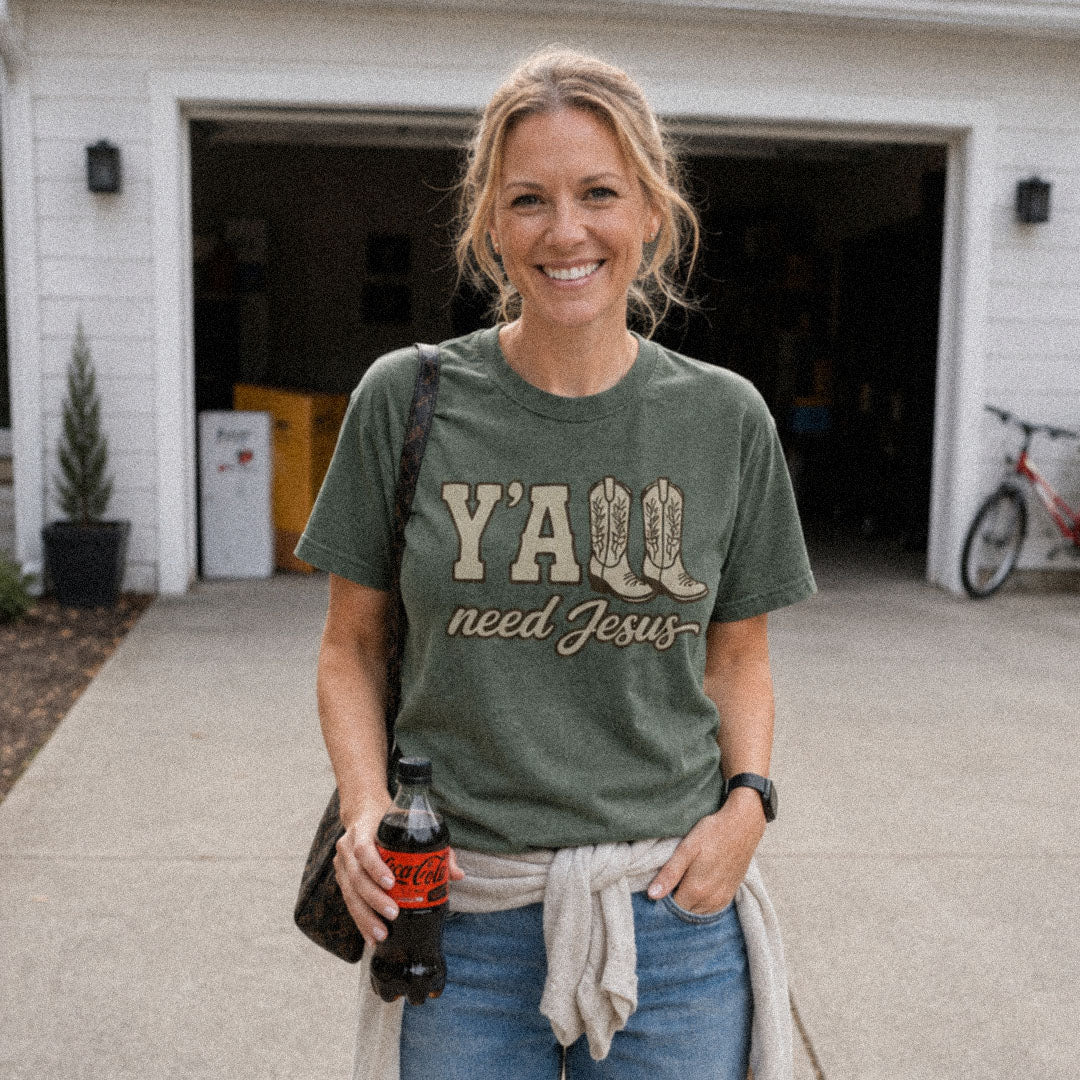 Woman on driveway wearing green (Moss) Comfort Colors® 1717 tshirt featuring a faith-inspired Y'all Need Jesus graphic with a Southern cowboy boots design.