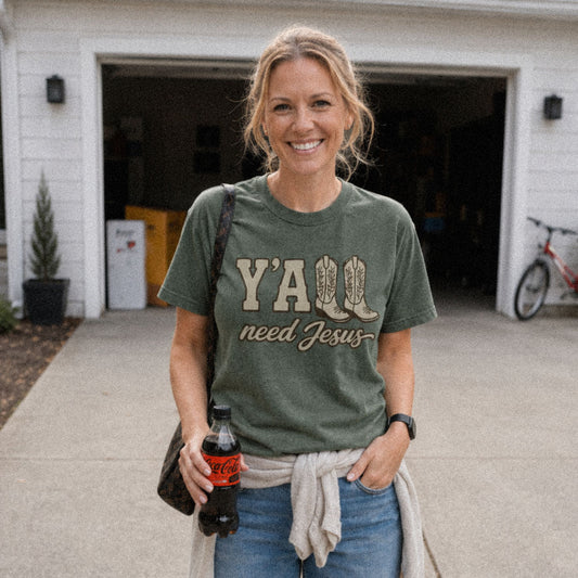 Woman on driveway wearing green (Moss) Comfort Colors® 1717 tshirt featuring a faith-inspired Y'all Need Jesus graphic with a Southern cowboy boots design.