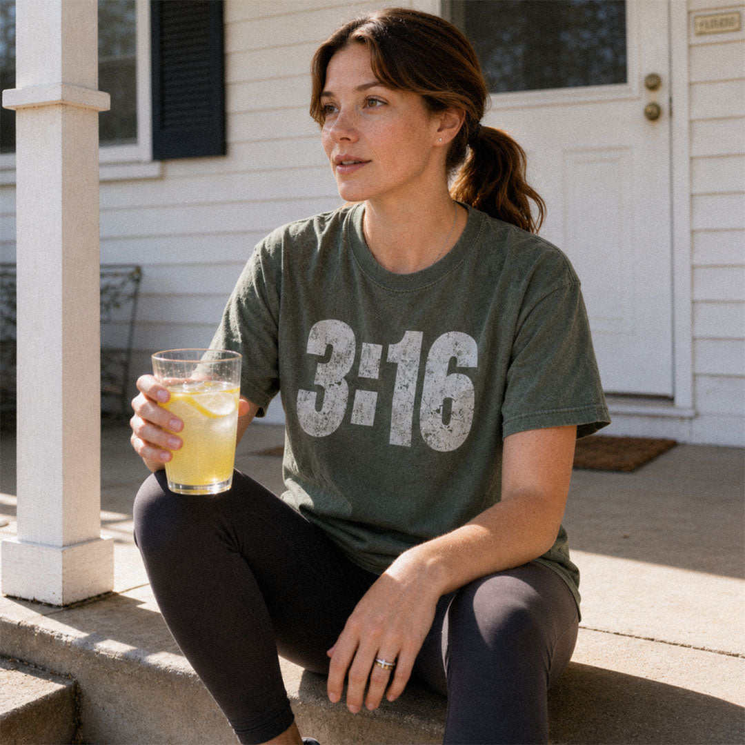 Woman on porch with lemonade wearing 3:16 scripture themed design on green (Moss) Comfort Colors 1717® tee.