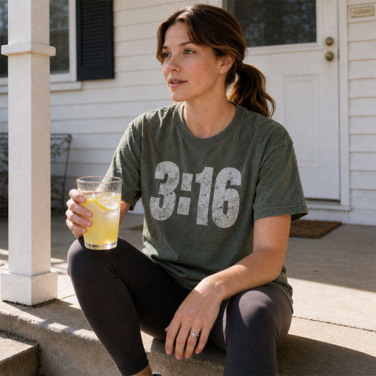 Woman on porch with lemonade wearing 3:16 scripture themed design on green (Moss) Comfort Colors 1717® tee.